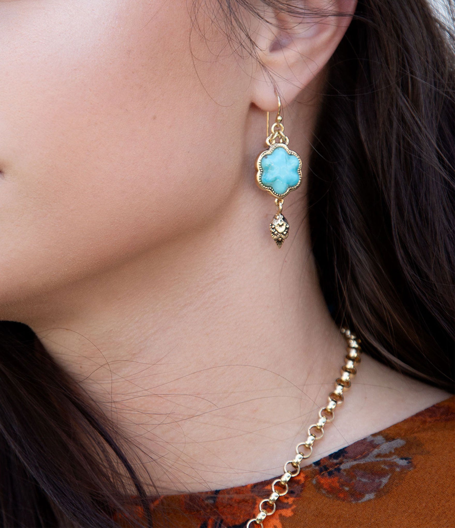 Close-up of a person wearing a gold earring with a blue gemstone.