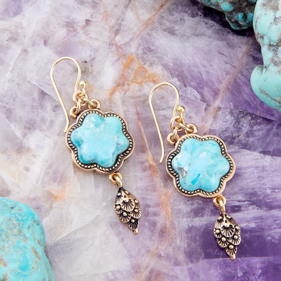 Turquoise earrings with gold and silver accents on a textured stone background