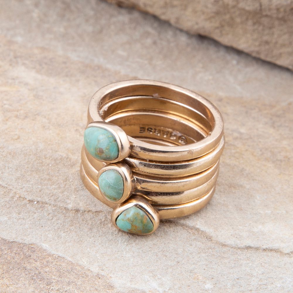 Stack of gold rings with turquoise stones on a stone surface