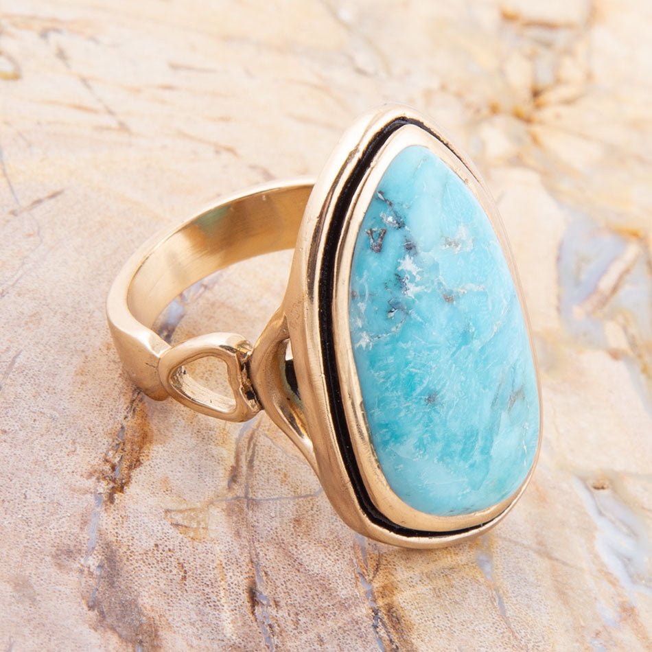 Gold ring with a large turquoise stone on a textured beige background