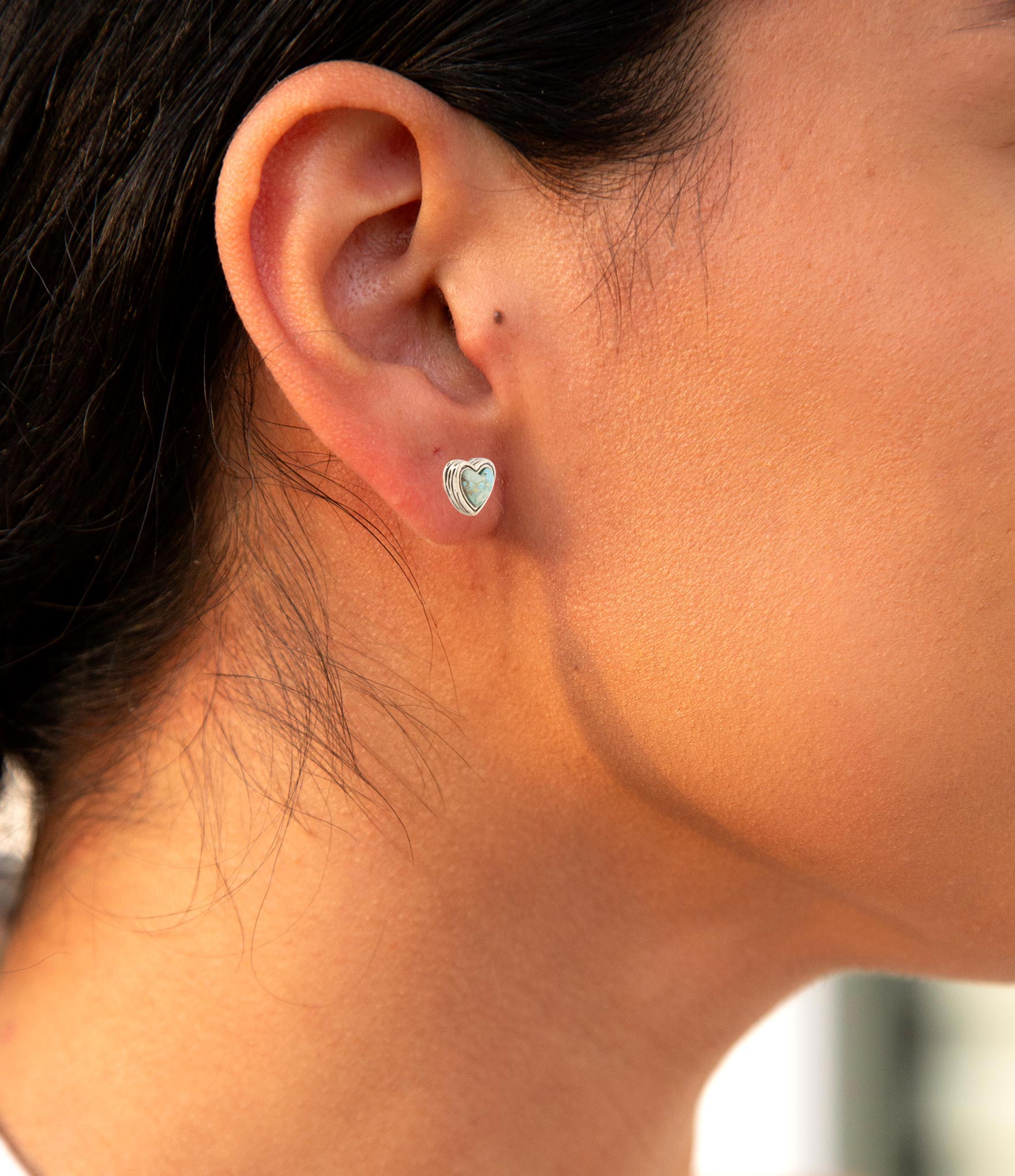 Close-up of an ear wearing a heart-shaped earring with a blurred background