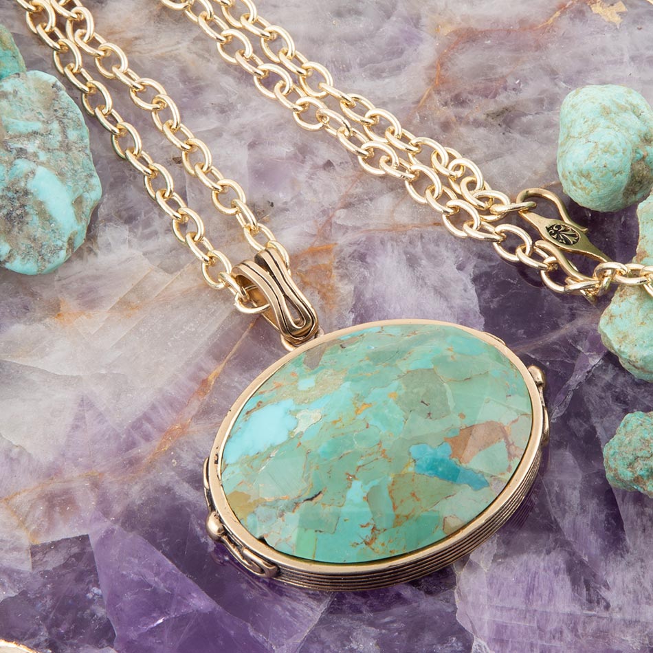 Gold necklace with a turquoise pendant on a textured purple surface