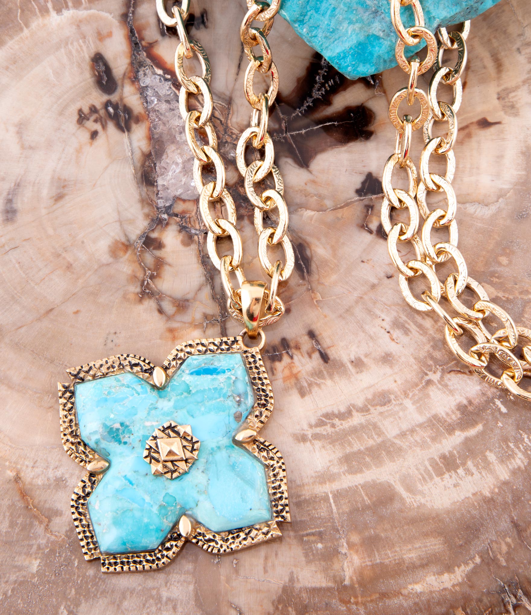 Gold chain necklace with a turquoise stone pendant on a textured surface