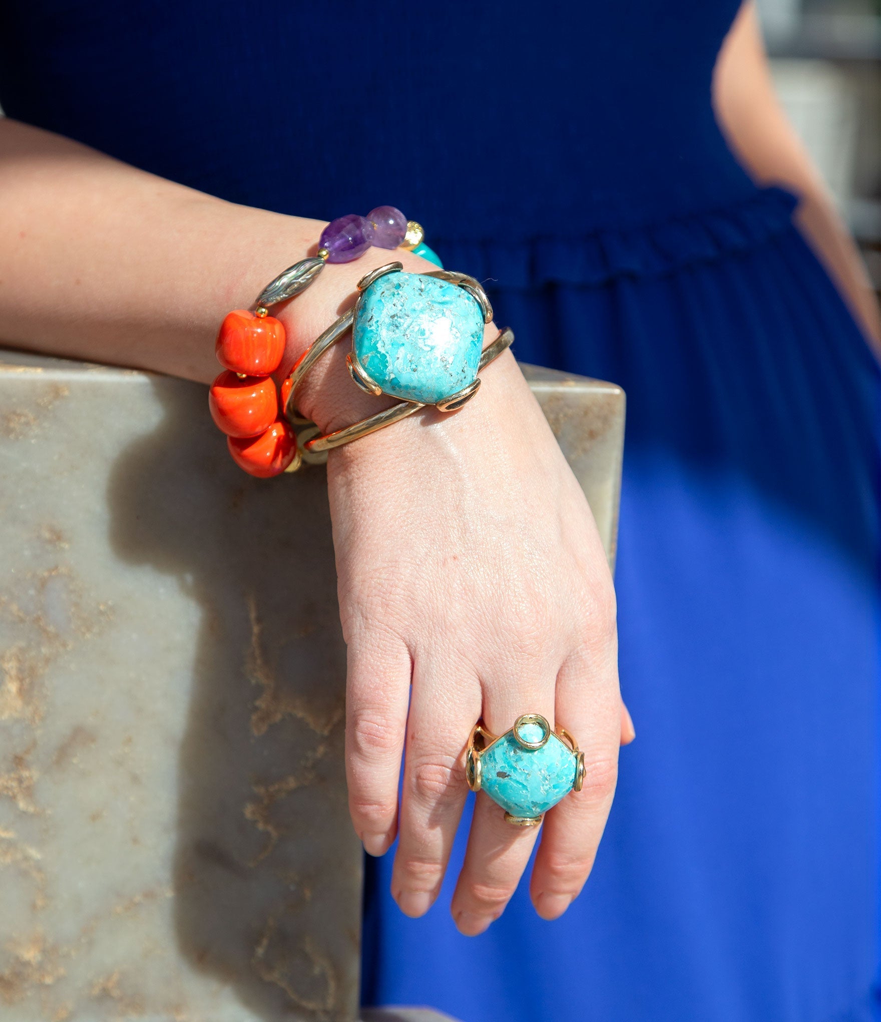 Close-up of a hand wearing colorful gemstone rings and bracelets on a blue dress background.