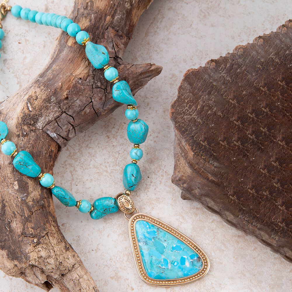 Turquoise beaded necklace with a gold pendant on a natural wood and stone background