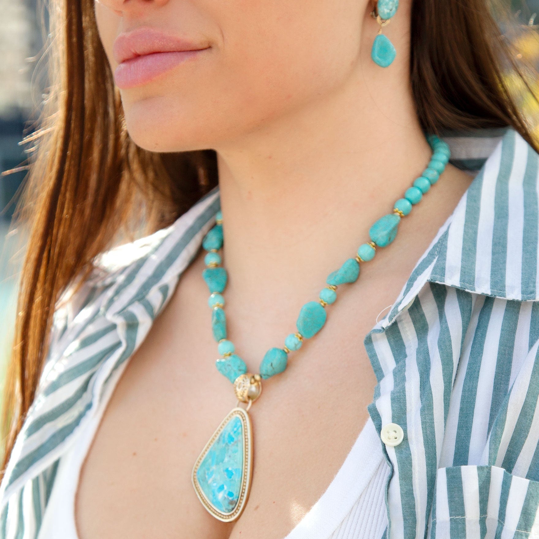 Woman wearing a turquoise necklace and earrings with a striped shirt.