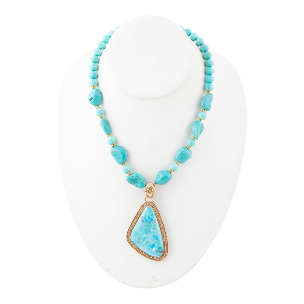 Turquoise beaded necklace with a large turquoise pendant on a white stand.