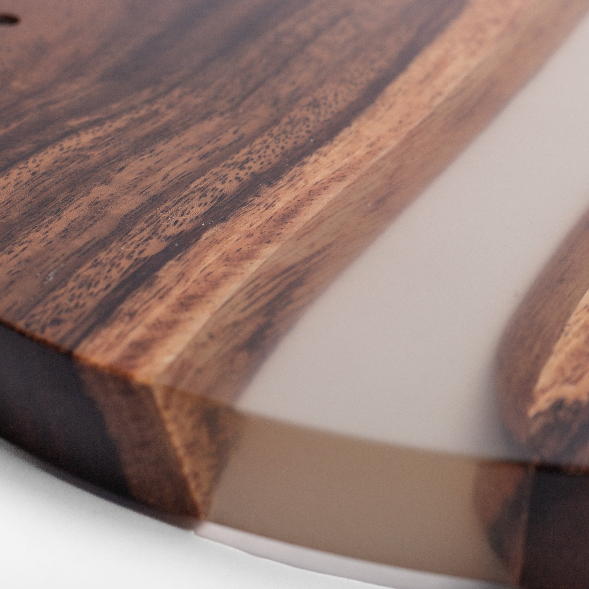 Close-up of a round wooden serving board with a live edge and a translucent beige resin inlay, showing detailed wood grain.