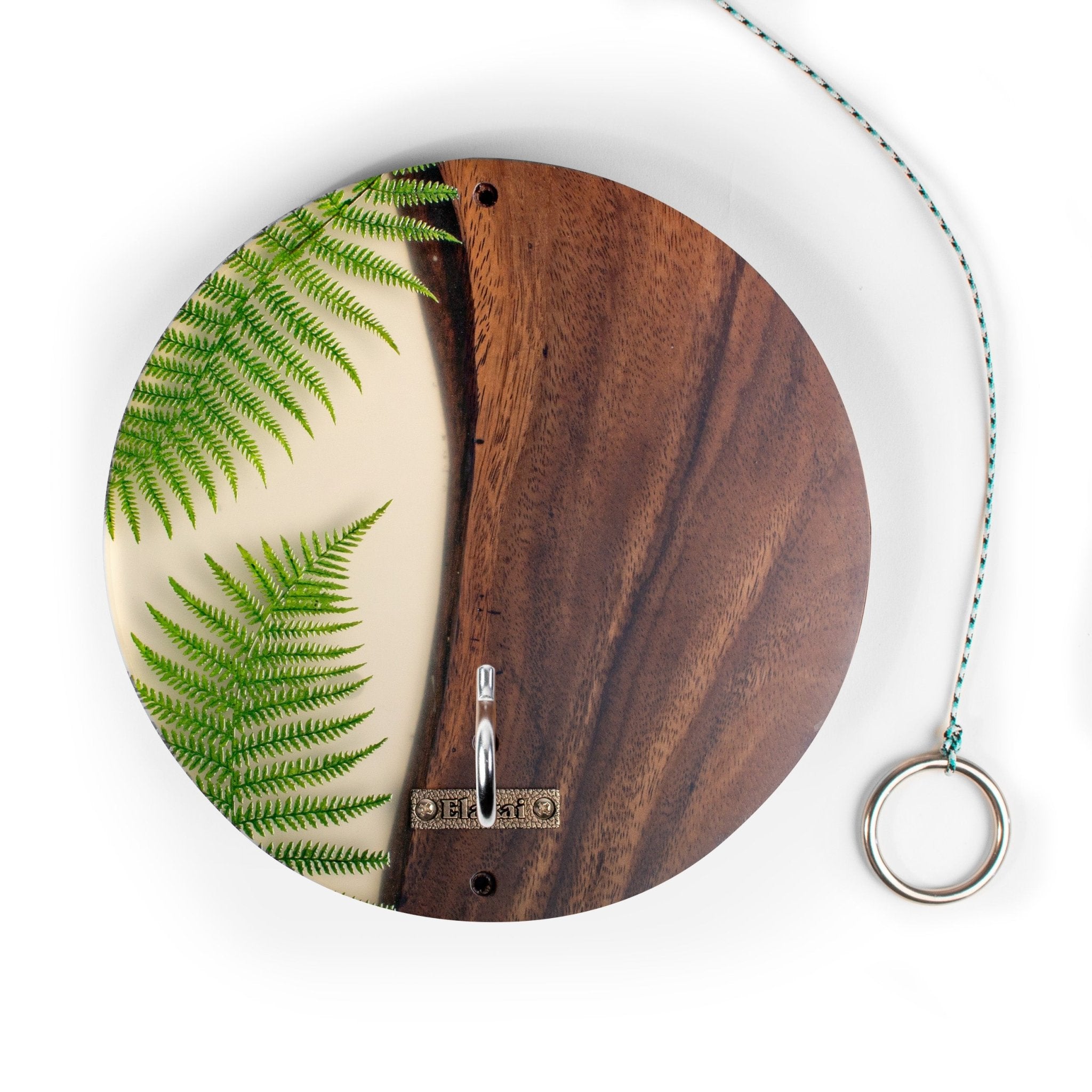Round wall hook with a split design featuring a green fern pattern on a cream background on the left and a dark brown wood grain pattern on the right, with a silver metal hook in the center and a hanging string with a ring on the right.