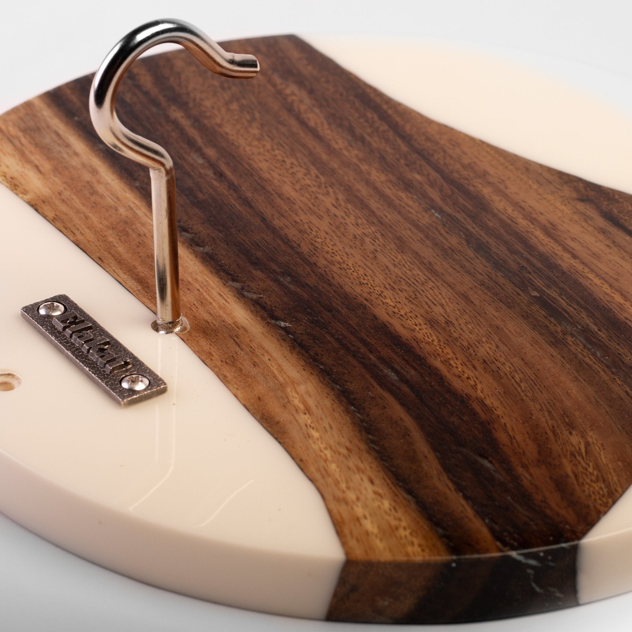 Close-up of a round wall hook with a dark brown wood-grain face and cream-colored edge, featuring a metal hook and a small branded plate.