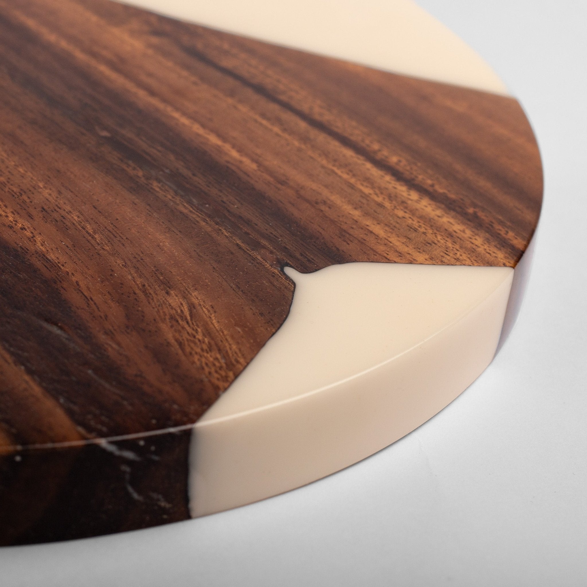 A close-up of a round wooden board or tray corner featuring a dark brown wood grain surface with a smooth, glossy cream-colored resin inlay.