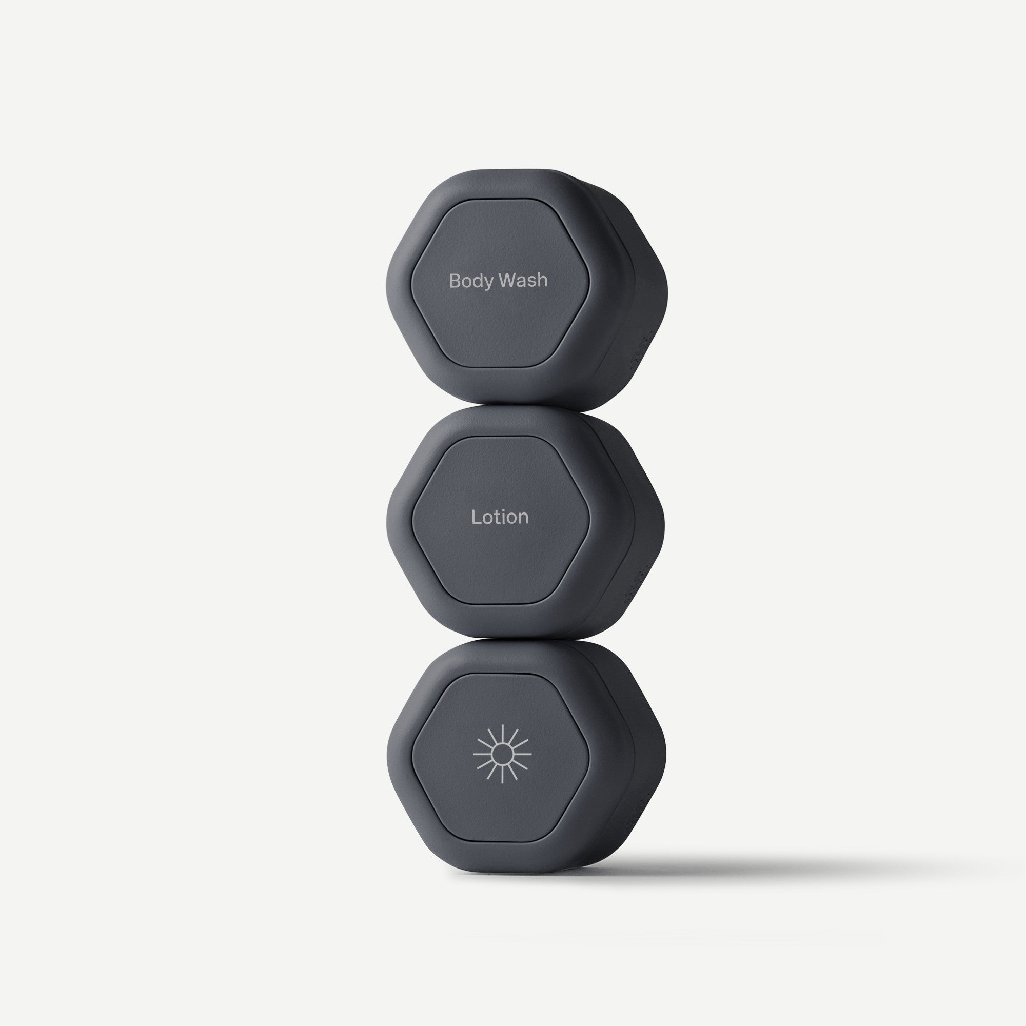 Three dark gray hexagonal personal care containers stacked vertically on a light gray background, labeled Body Wash, Lotion, and Sunscreen with simple white icons and text.