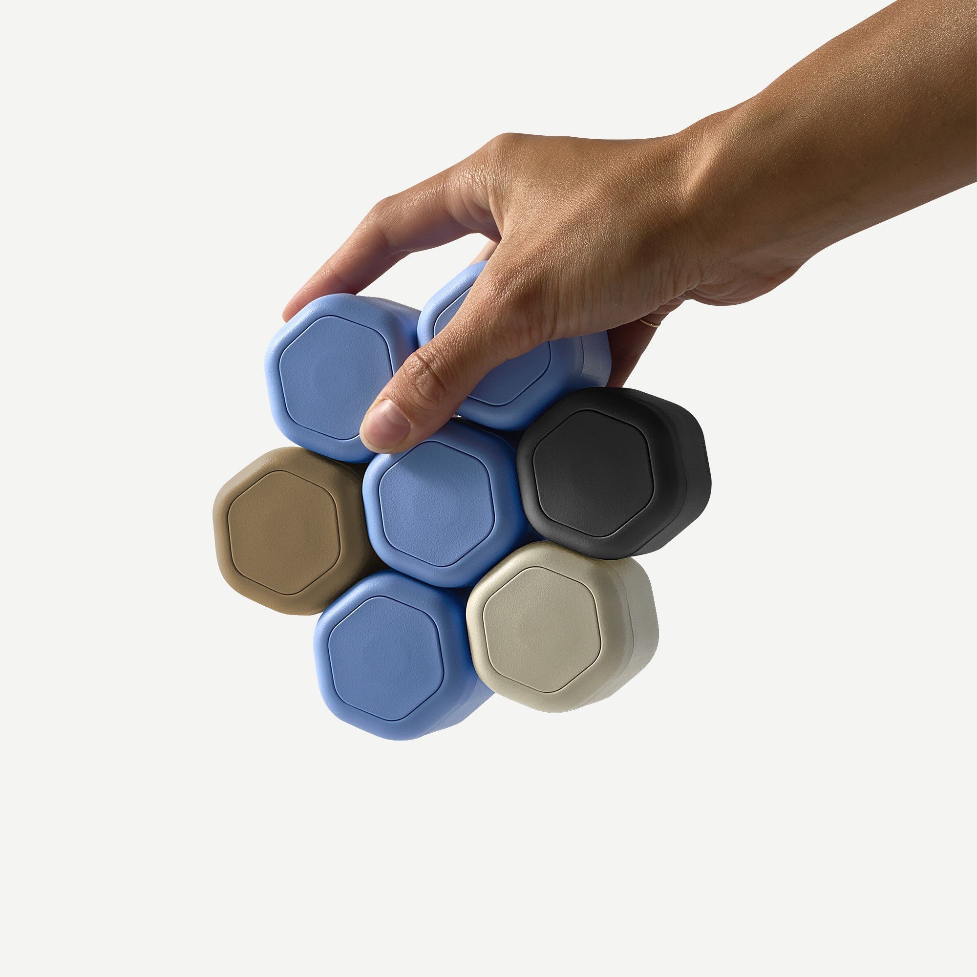 Hand holding a stack of hexagonal containers in various colors on a white background