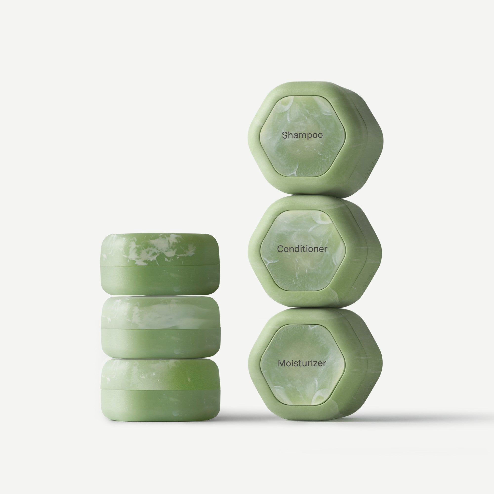 Stack of green hexagonal soap bars labeled 'Shampoo', 'Conditioner', and 'Moisturizer' on a white background.