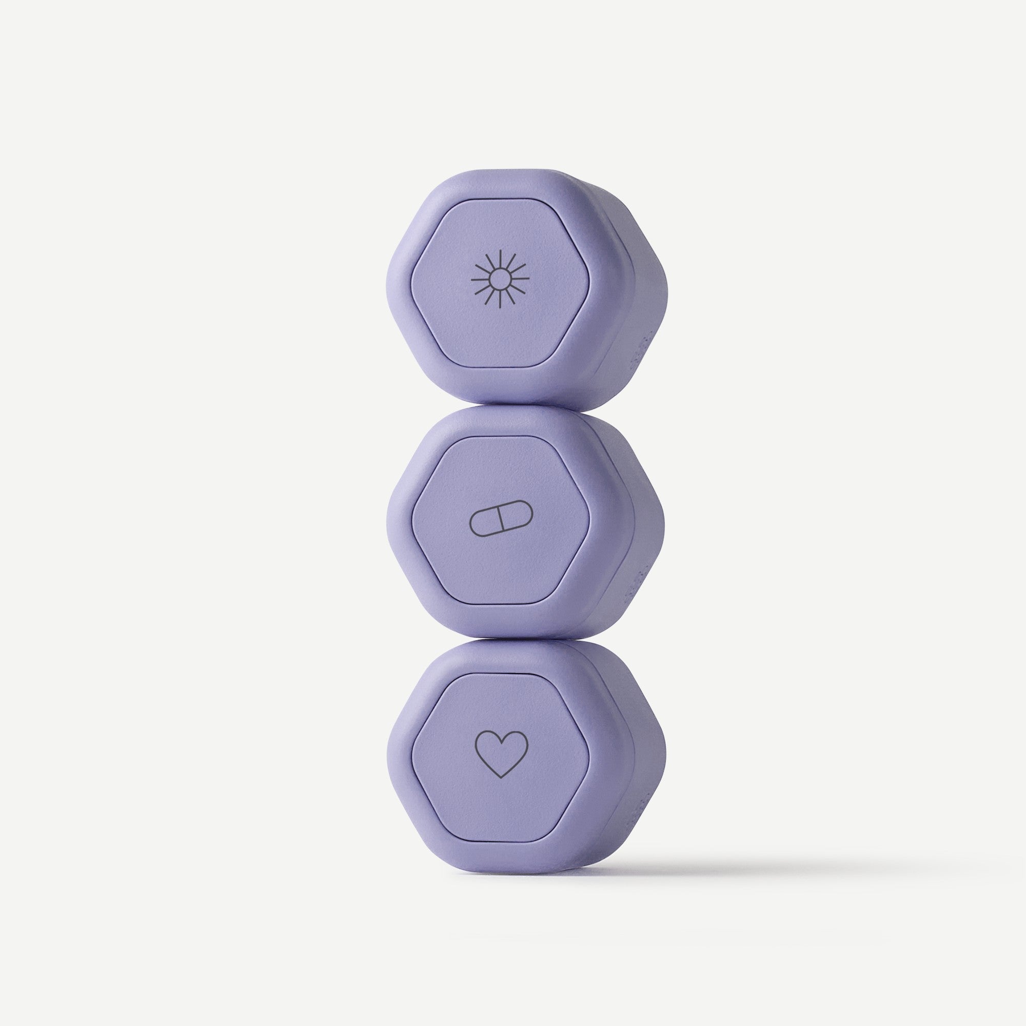Three lavender hexagonal pill boxes stacked vertically on a clean white background, each featuring a different minimalist icon on top: a sun, a capsule, and a heart.