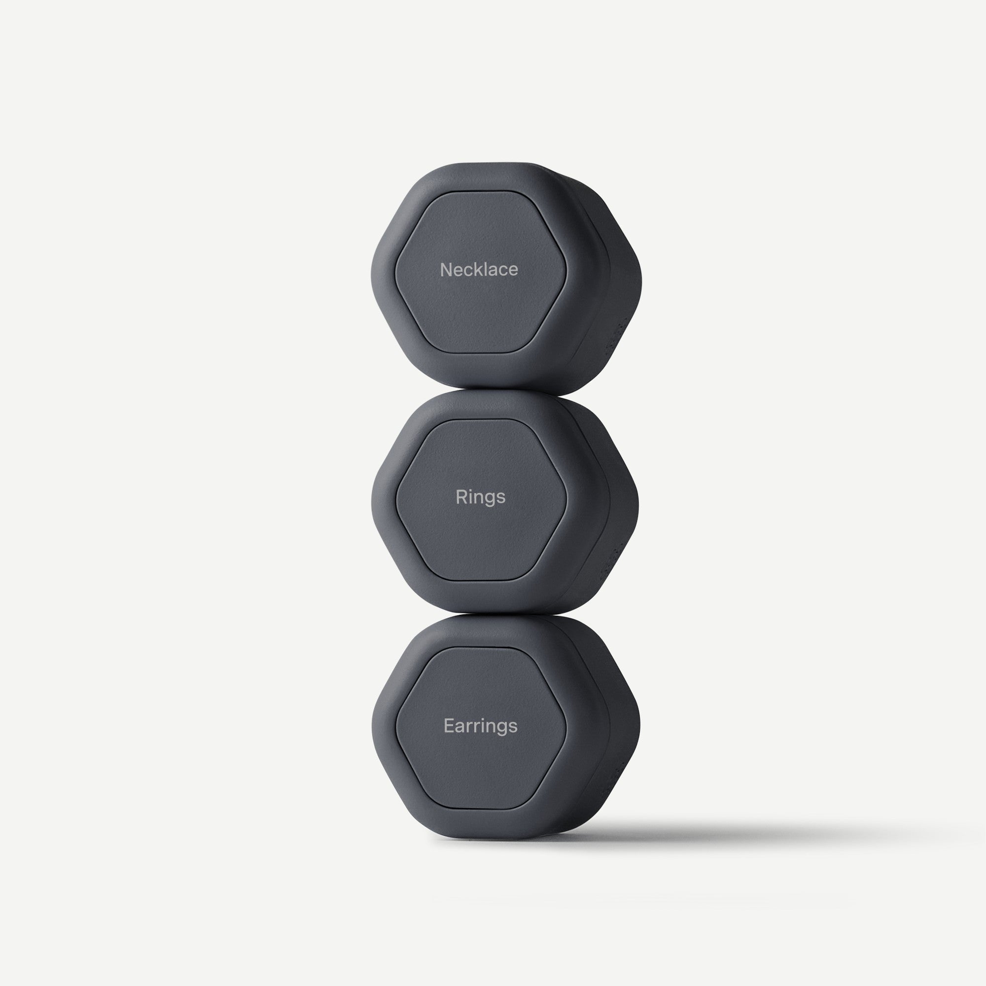 Three dark gray hexagonal product tags stacked vertically on a light gray background, labeled 'Necklace', 'Rings', and 'Earrings'.