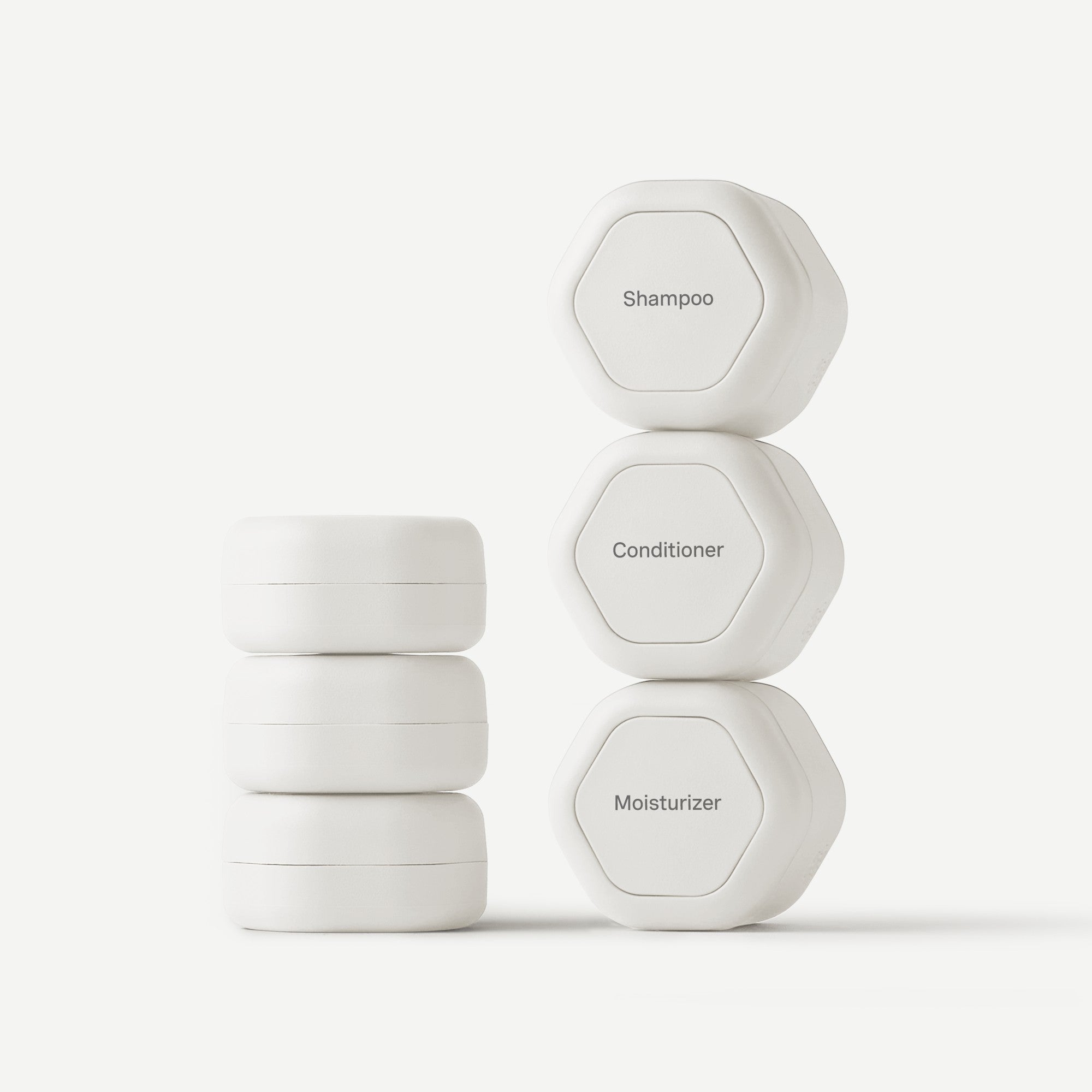 Stack of white hexagonal containers labeled 'Shampoo', 'Conditioner', and 'Moisturizer' on a light gray background.