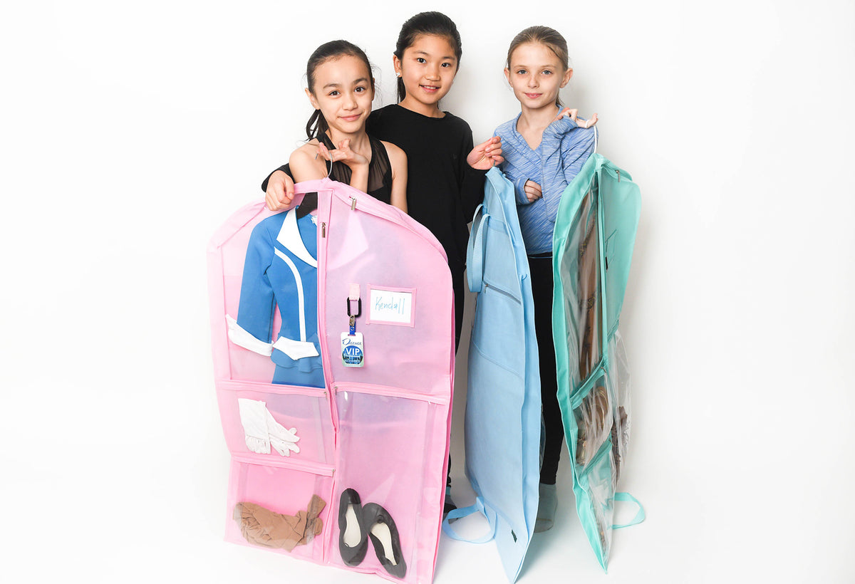 Three children standing behind two large transparent garment storage bags, one pink and one light blue, against a plain white background.