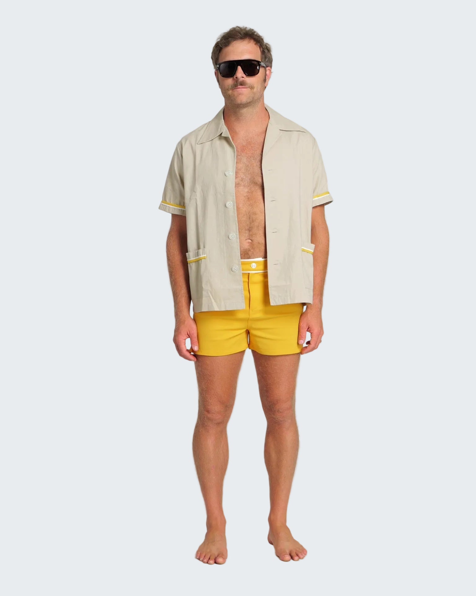 Man wearing a beige shirt with yellow trim and yellow swim shorts on a white background