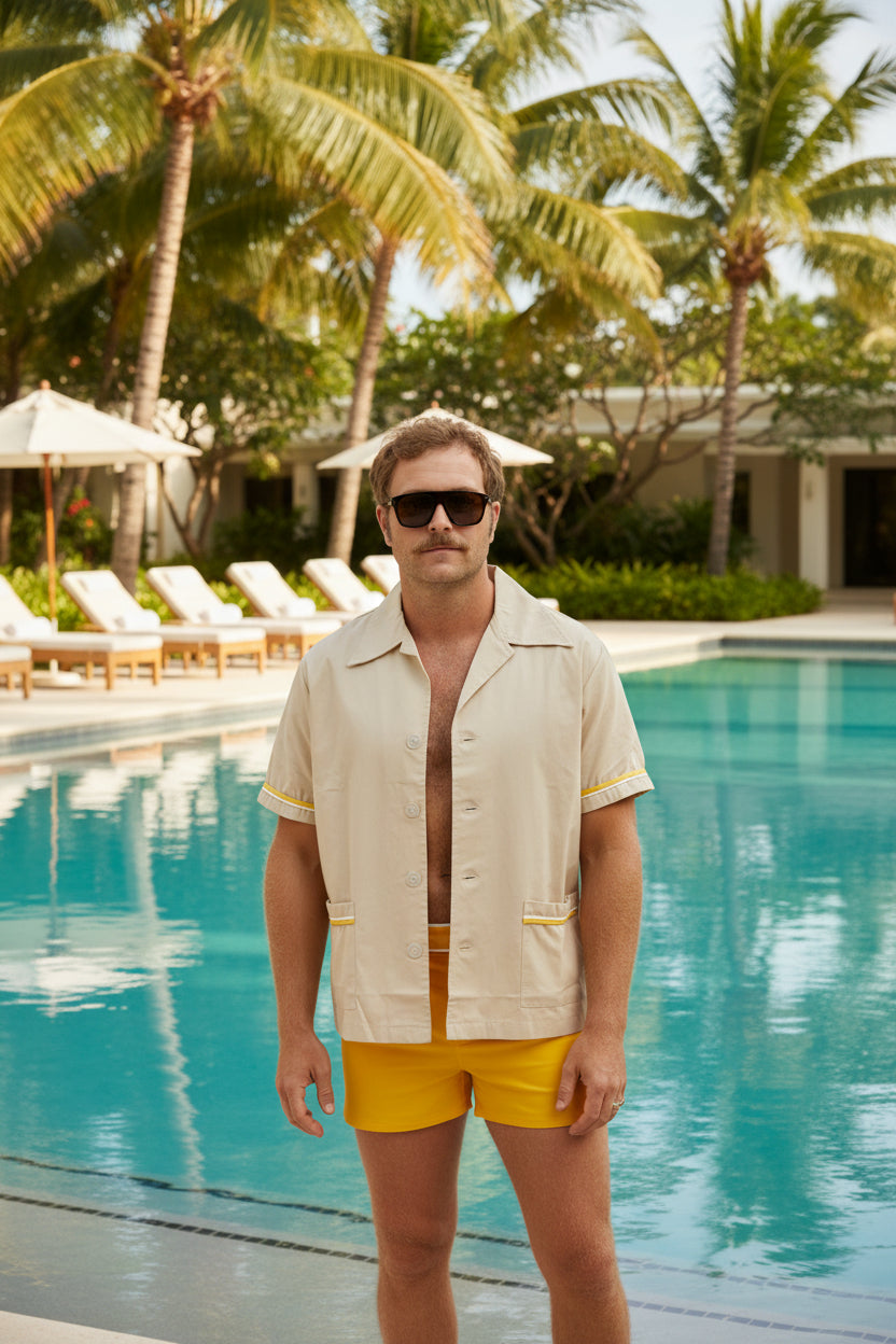 Man wearing a beige shirt with yellow accents and yellow swim shorts on a white background