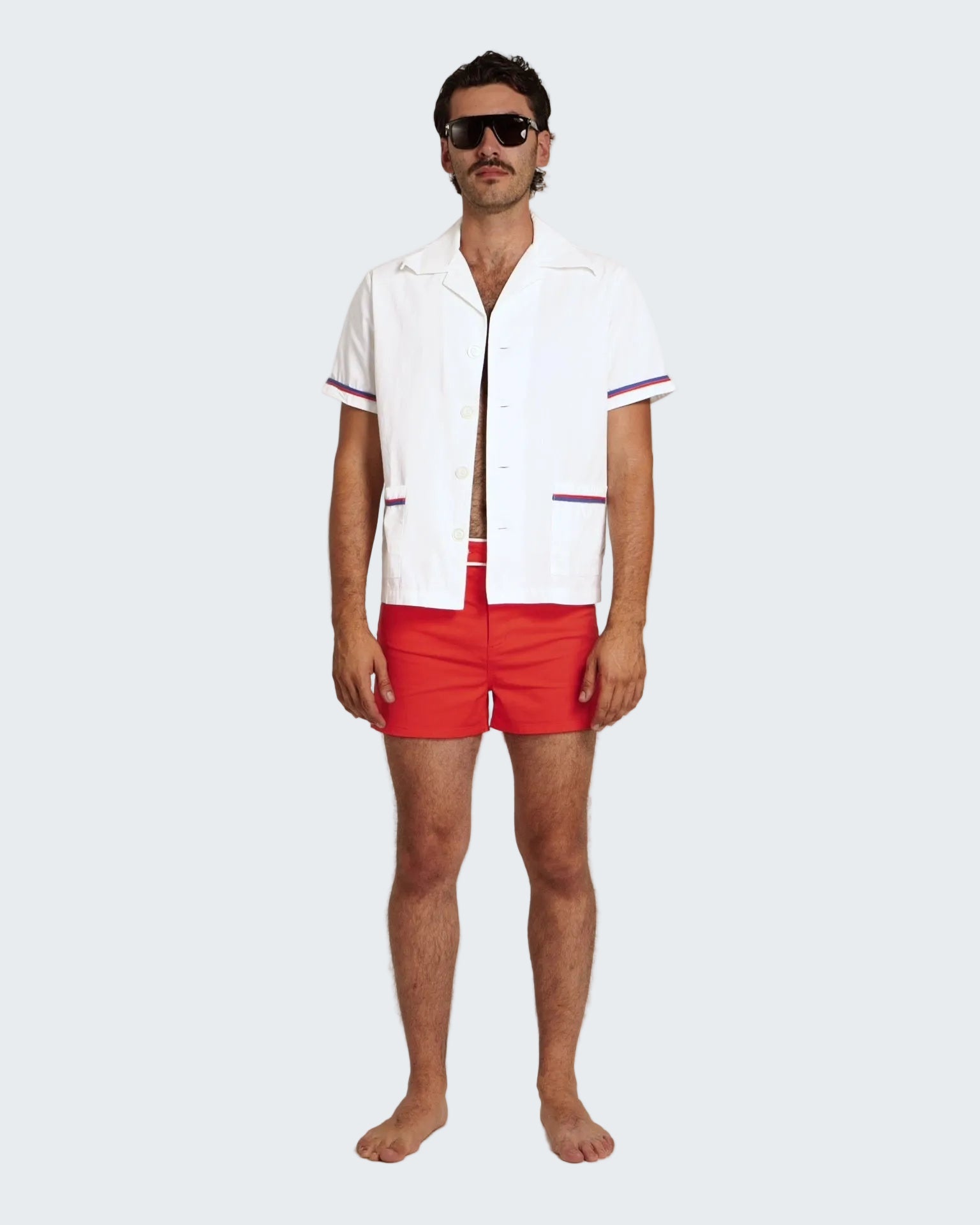 Man wearing a white shirt with red trim and red swim shorts on a white background