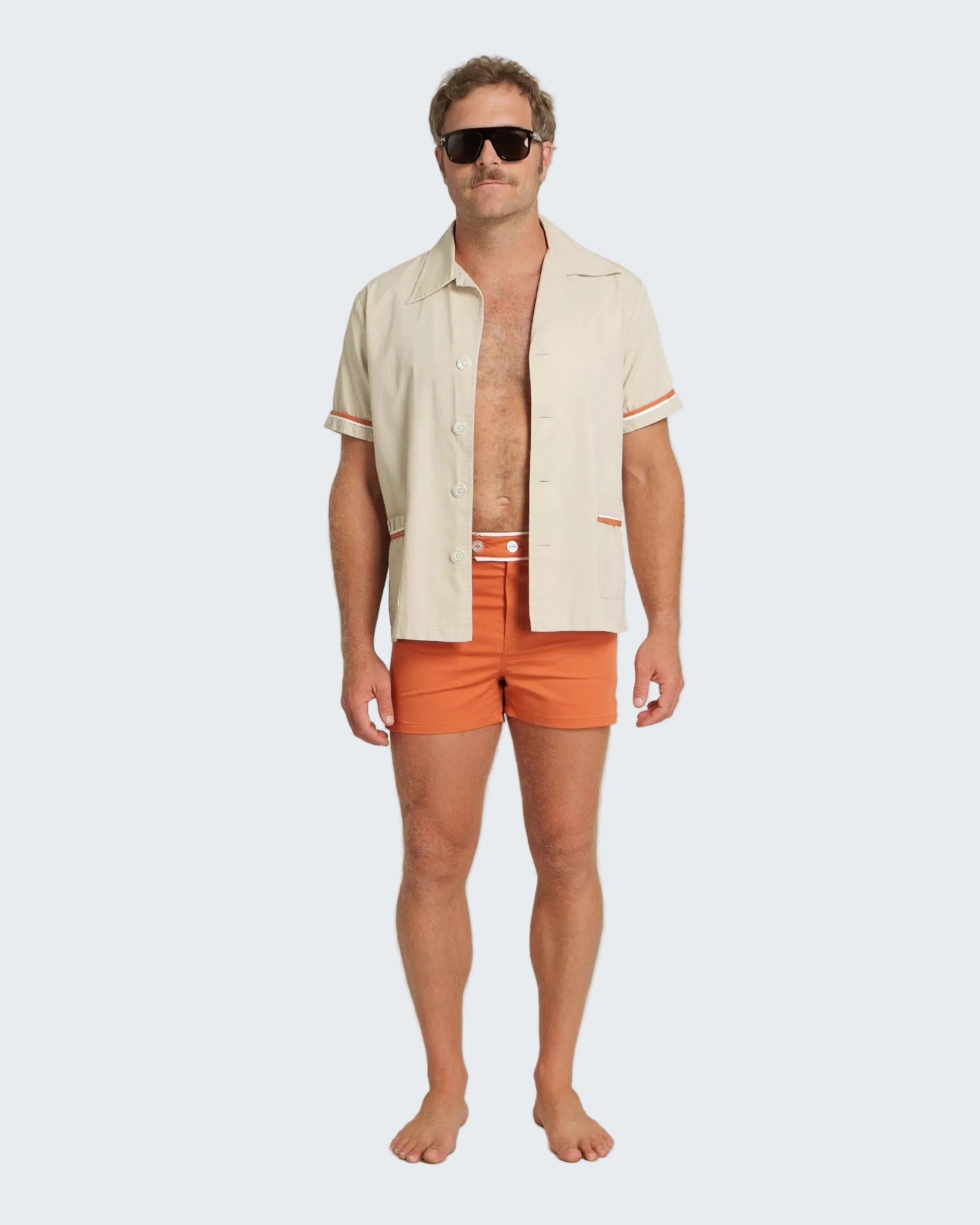 Man wearing a beige shirt and orange swim shorts on a white background