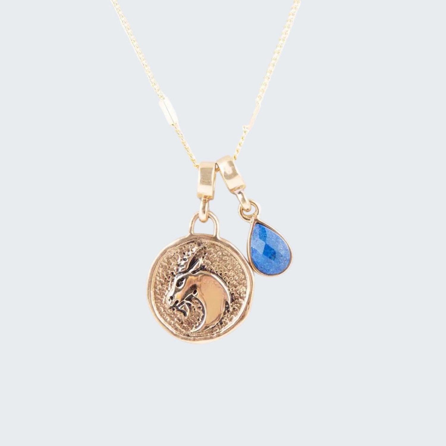 Gold necklace with a horse head pendant and blue teardrop charm on a white background