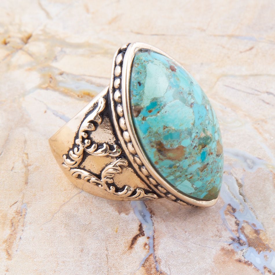 Turquoise stone ring with gold detailing on a textured beige surface