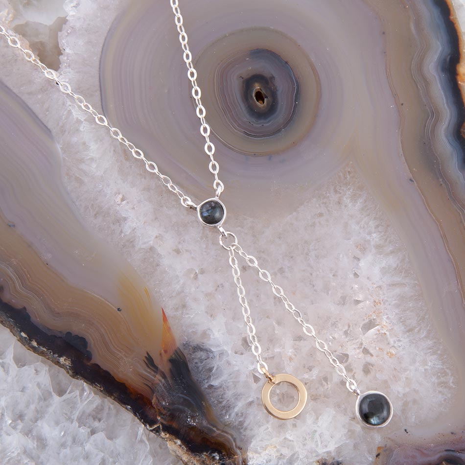 Silver necklace with black and gold elements on a textured stone surface
