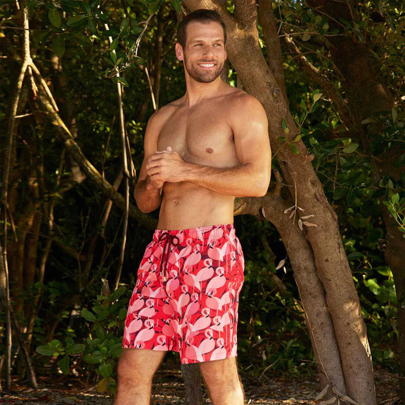 Man wearing red swim shorts with flamingo pattern standing in a natural setting.