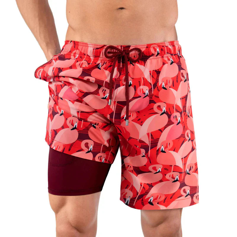 Red swim shorts with flamingo pattern worn by a person on a white background