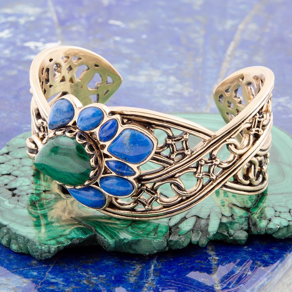 Gold bracelet with blue and green stones on a green stone surface