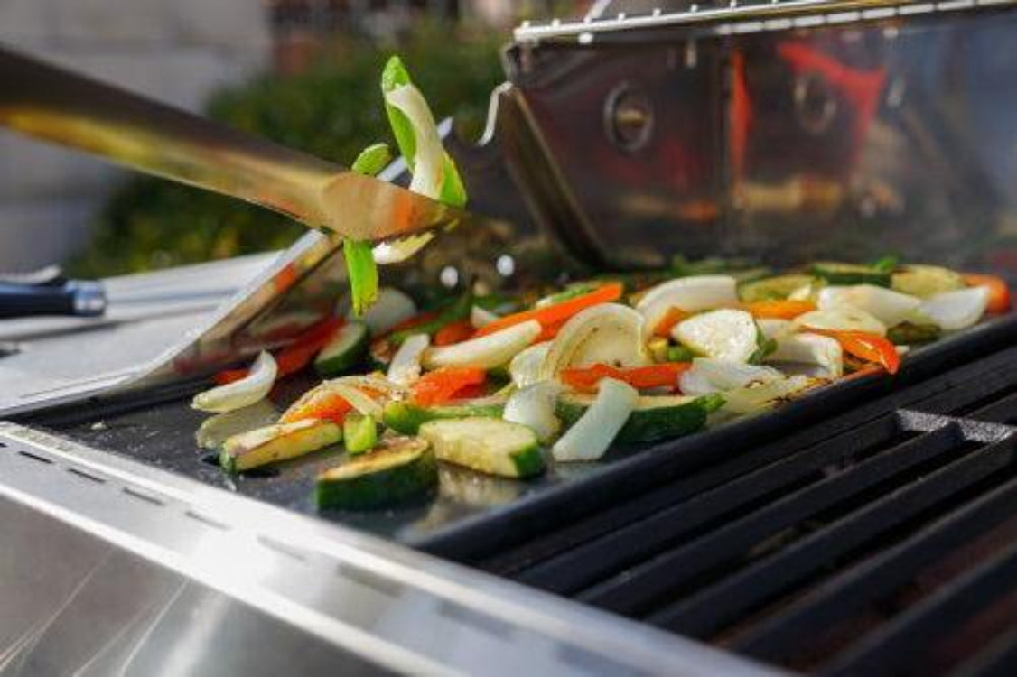 Vegetables being grilled on a barbecue with tongs