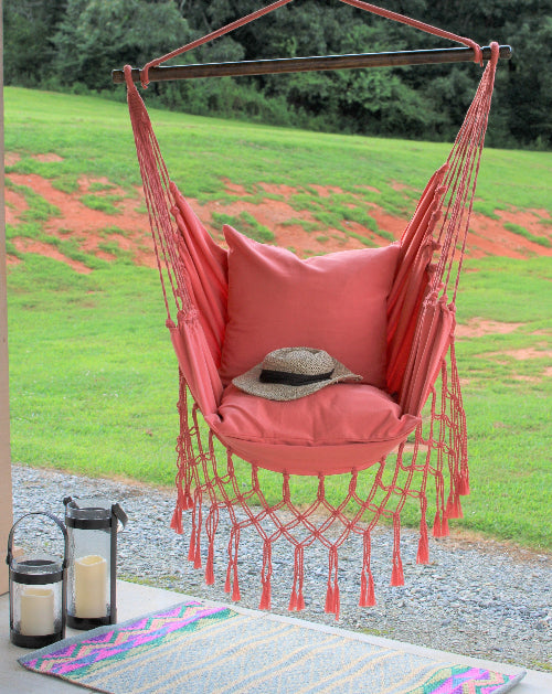 Coral hammock chair with cushions and a hat in a garden setting
