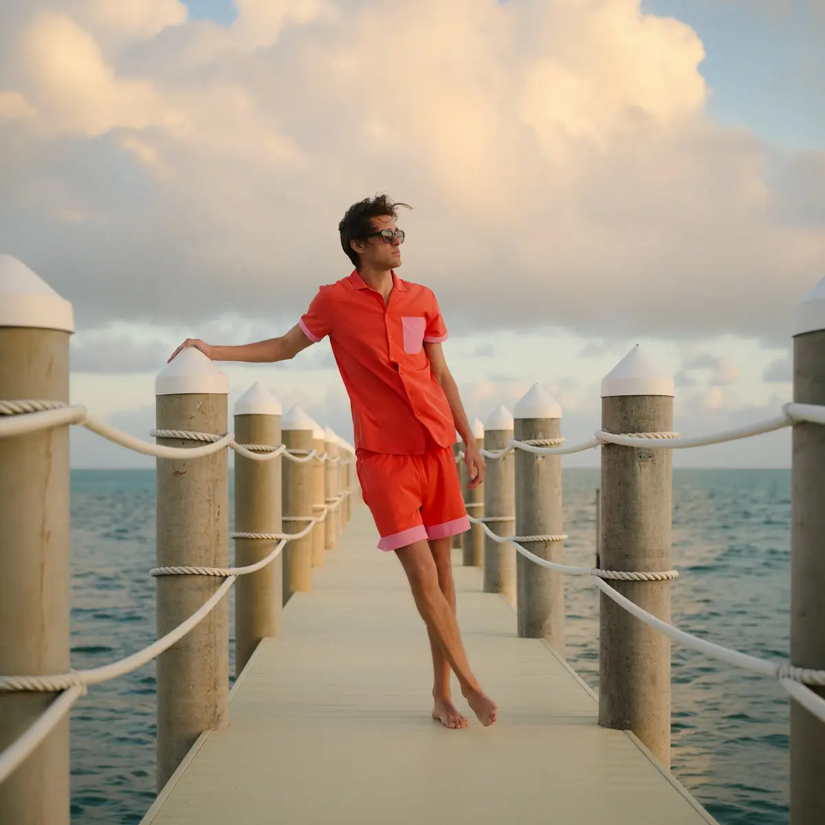 Person in a red outfit standing on a wooden pier with ocean and sky background