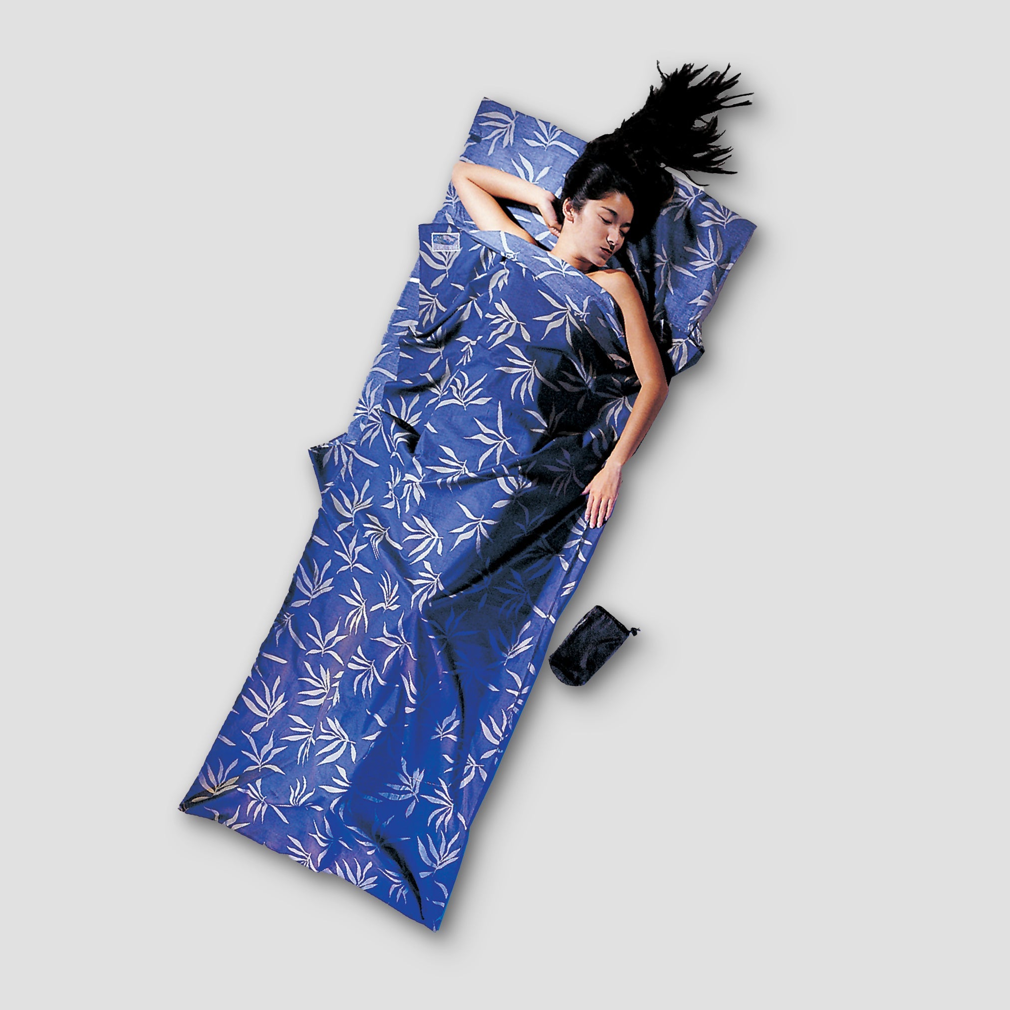 Person lying on a blue floral-patterned sleeping bag against a gray background