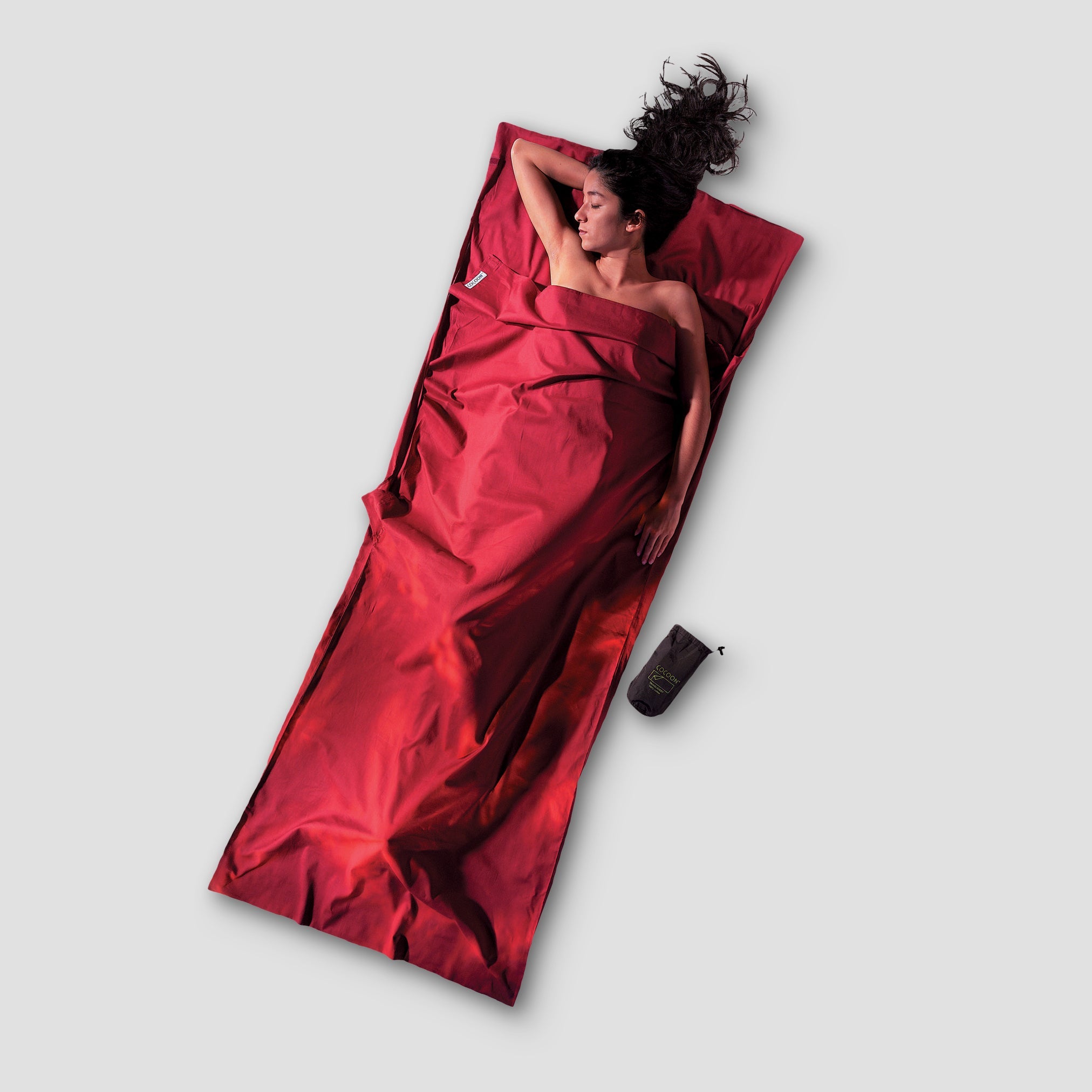 Person lying on a red satin sheet with a matching bag on a light gray background
