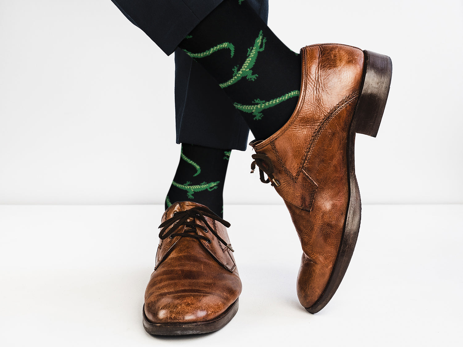 Brown dress shoes and black pants with green patterns on a white background