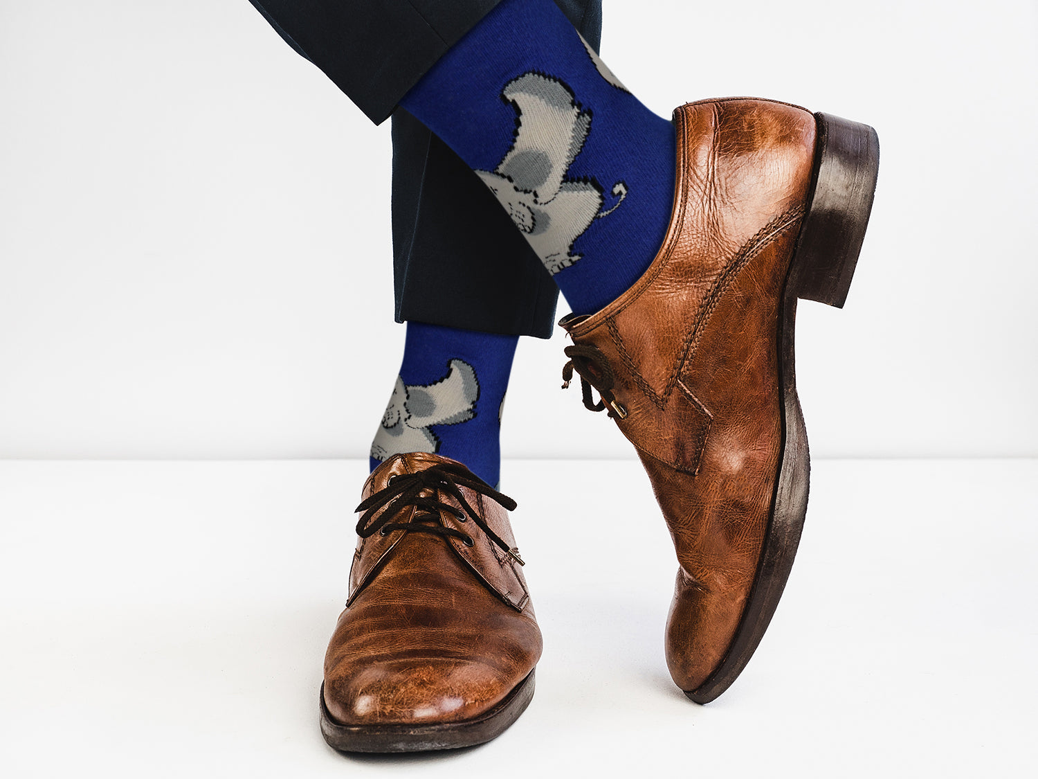 Brown leather shoes and blue socks with elephant design on a white background