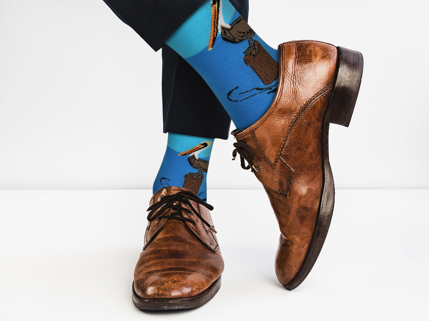Brown dress shoes and blue socks with a design worn by a person on a white background