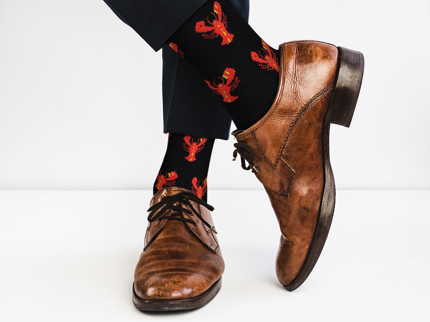 Brown dress shoes and black socks with red lobster pattern on a white background