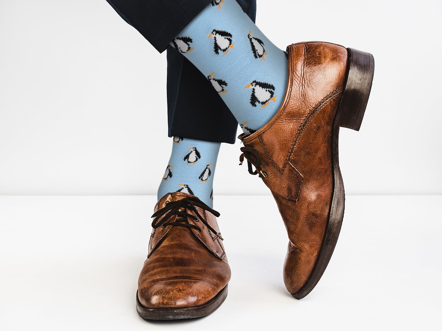 Brown dress shoes with blue socks featuring penguin pattern on a white background