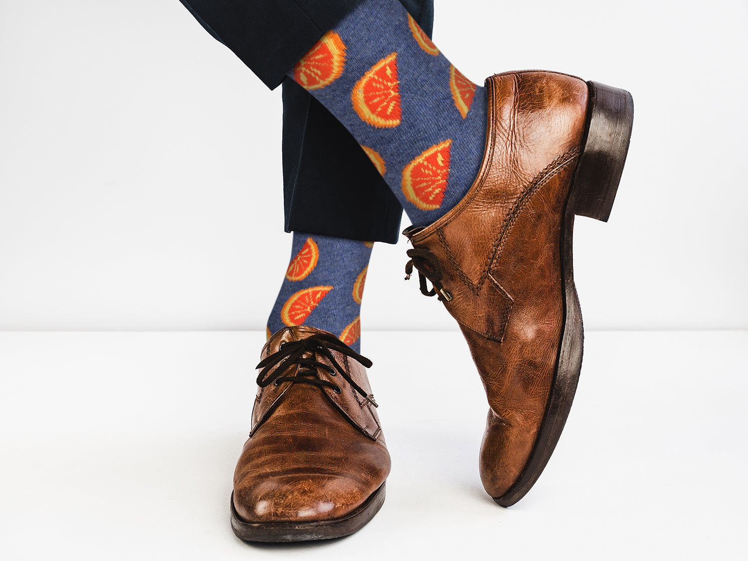 Brown dress shoes and blue socks with orange pattern on a white background