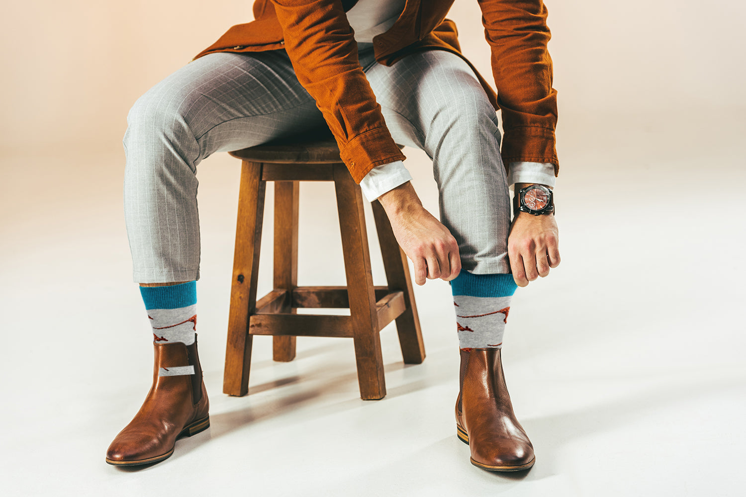 Person sitting on a stool wearing brown boots, light gray pants, and patterned socks.