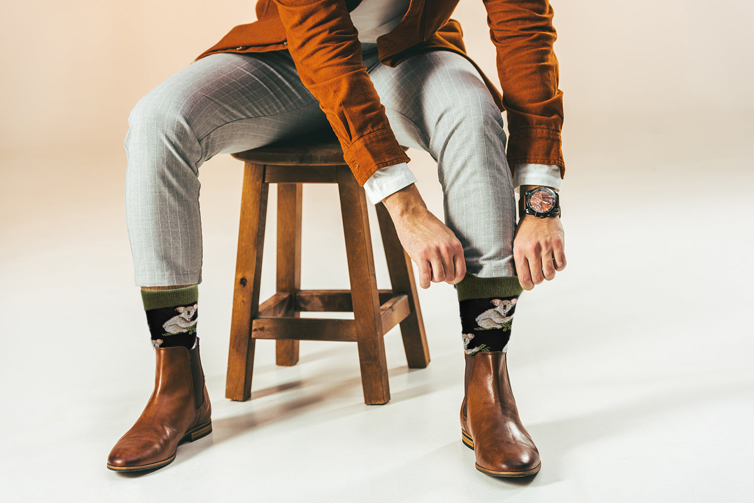 Person wearing brown boots, light gray pants, and patterned socks sitting on a wooden stool.