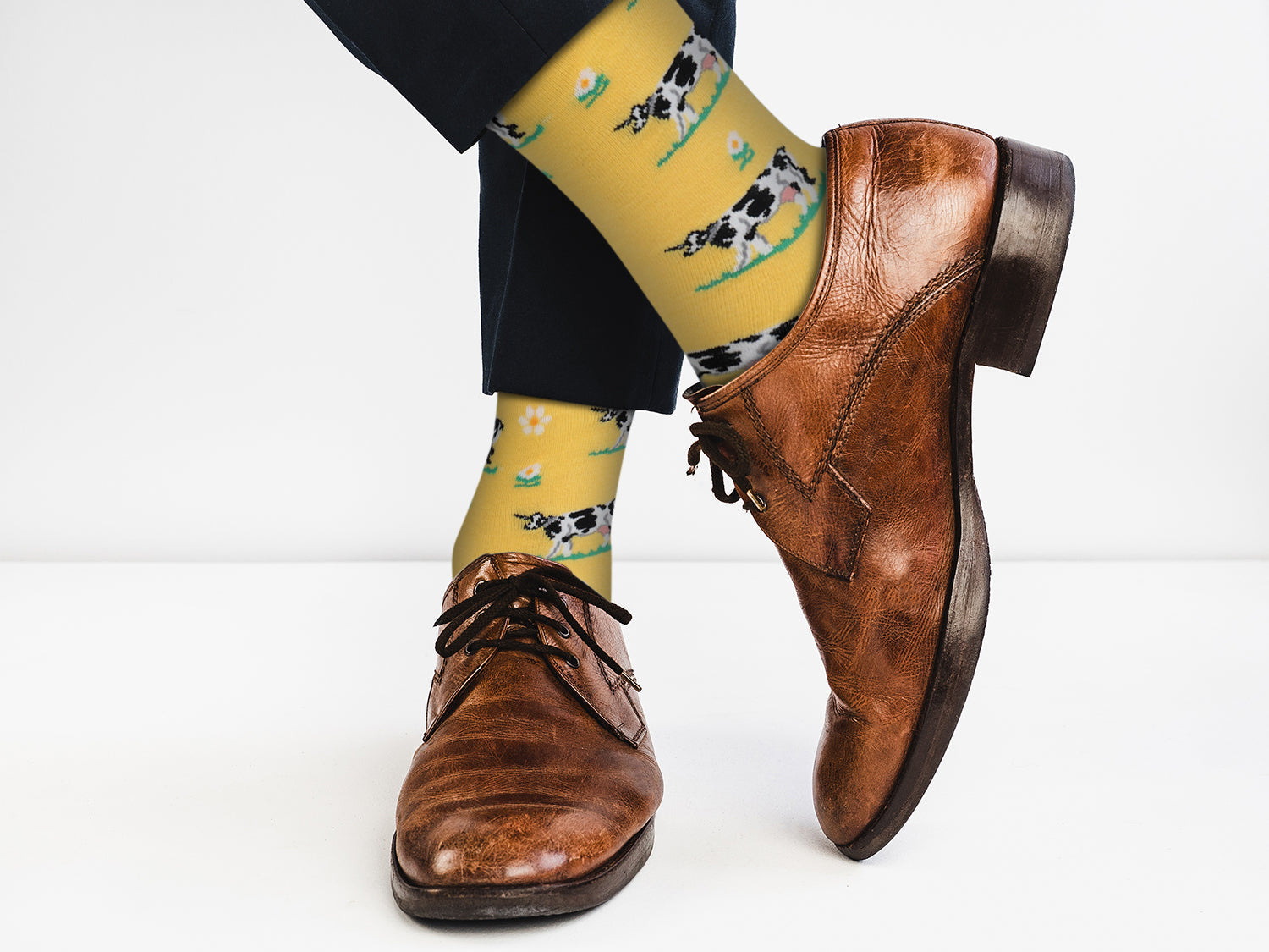 Brown leather shoes with yellow socks featuring cow patterns on a white background