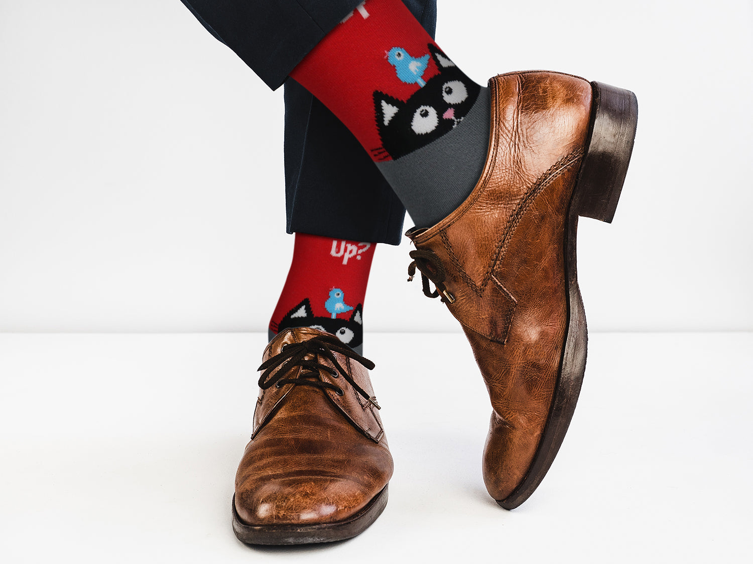 Brown dress shoes with red socks featuring black cat designs on a white background