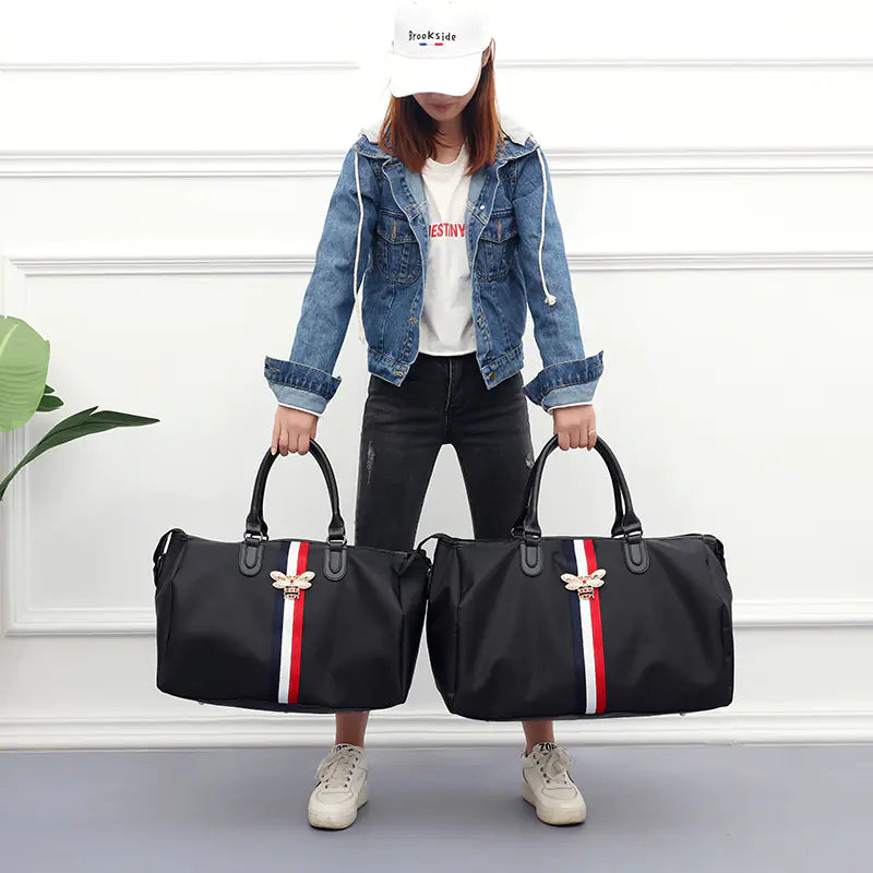 Person holding two black duffel bags with red and white stripes against a white wall.