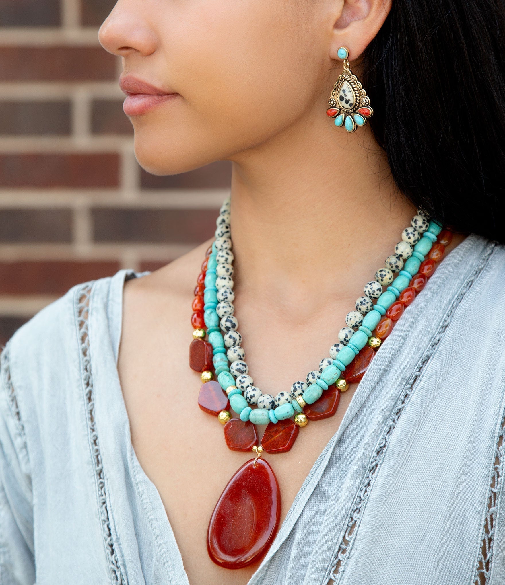 Close-up of a person wearing a colorful beaded necklace and earrings against a brick wall.