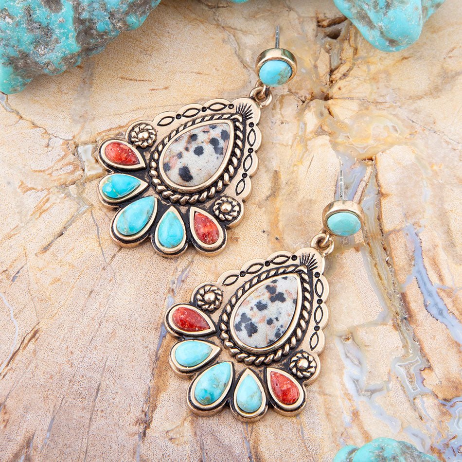 Pair of ornate earrings with turquoise and red stones on a stone surface